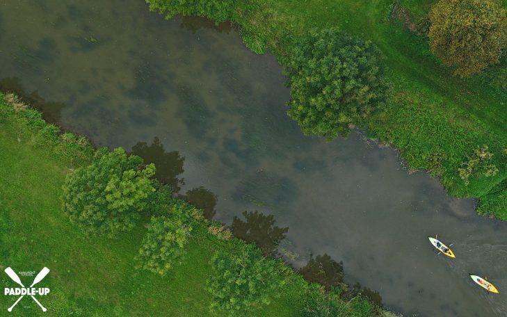 Zwei Kajaks auf einem ruhigen Fluss umgeben von grünem Uferland.