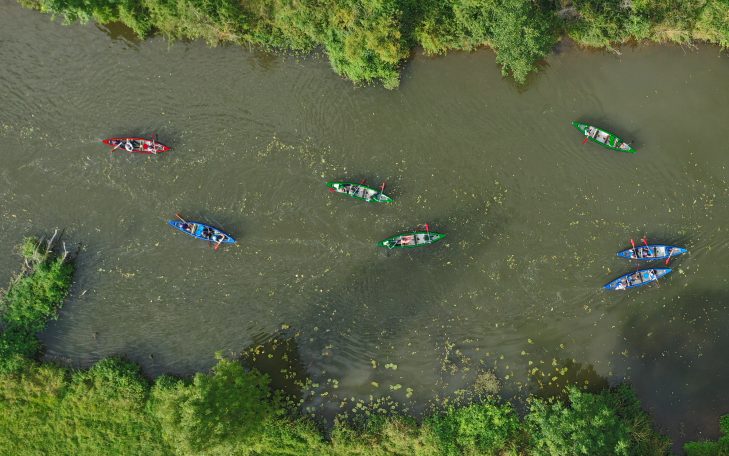Blick von oben auf Kanus, die in einem ruhigen Fluss umgeben von Bäumen paddeln.