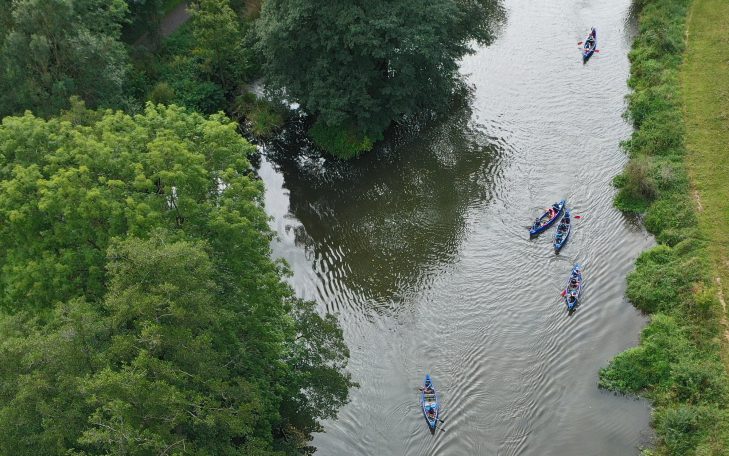 Grüne Ufer mit Kanufahrern auf einem ruhigen Fluss.