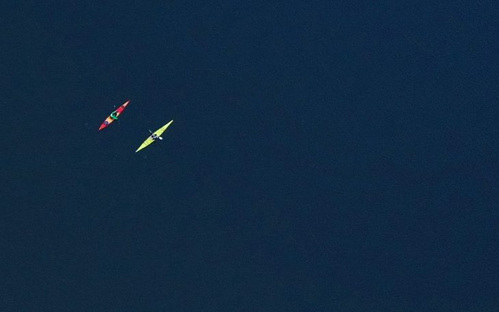 Zwei Kanus, eines rot und eines gelb, auf ruhigem Wasser vor dunklem Hintergrund.