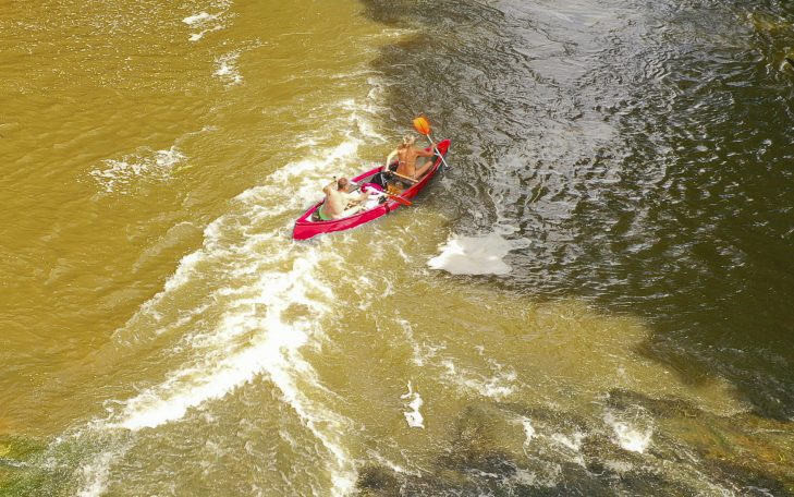 Roter Kajak auf einem Fluss mit welliger Wasseroberfläche.