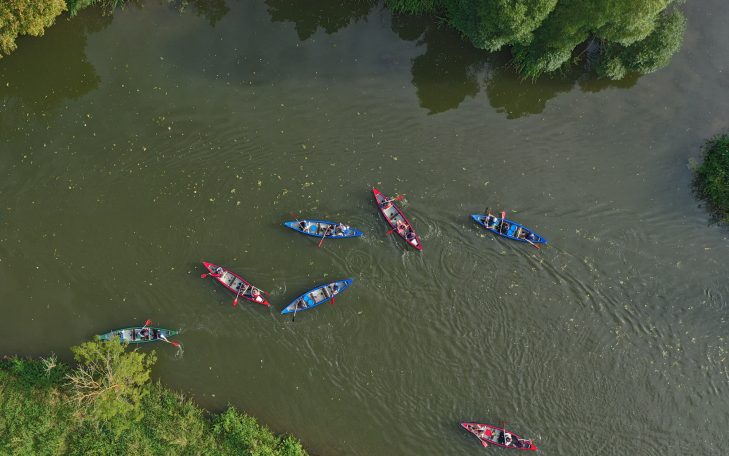 Mehrere Kanus in roten und blauen Farben auf einem ruhigen Fluss umgeben von Bäumen.