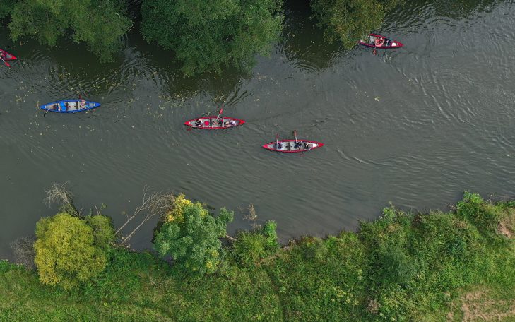 Mehrere Kajaks in roter und blauer Farbe auf einem ruhigen Fluss mit grüner Ufervegetation.